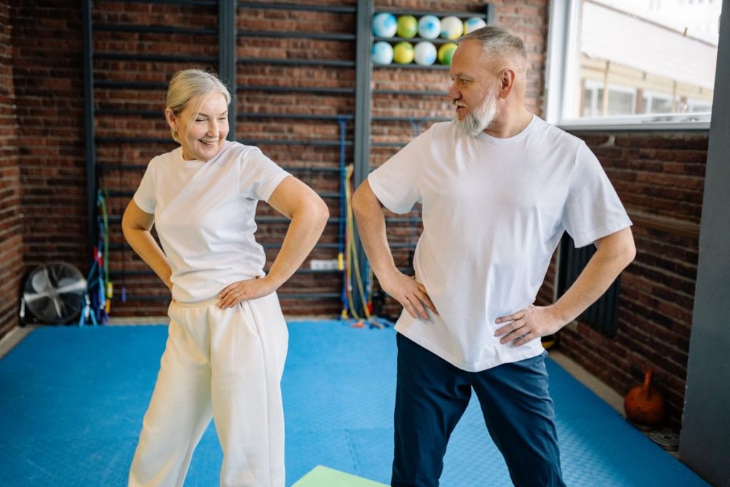 An older couple smiling as they exercise together at home